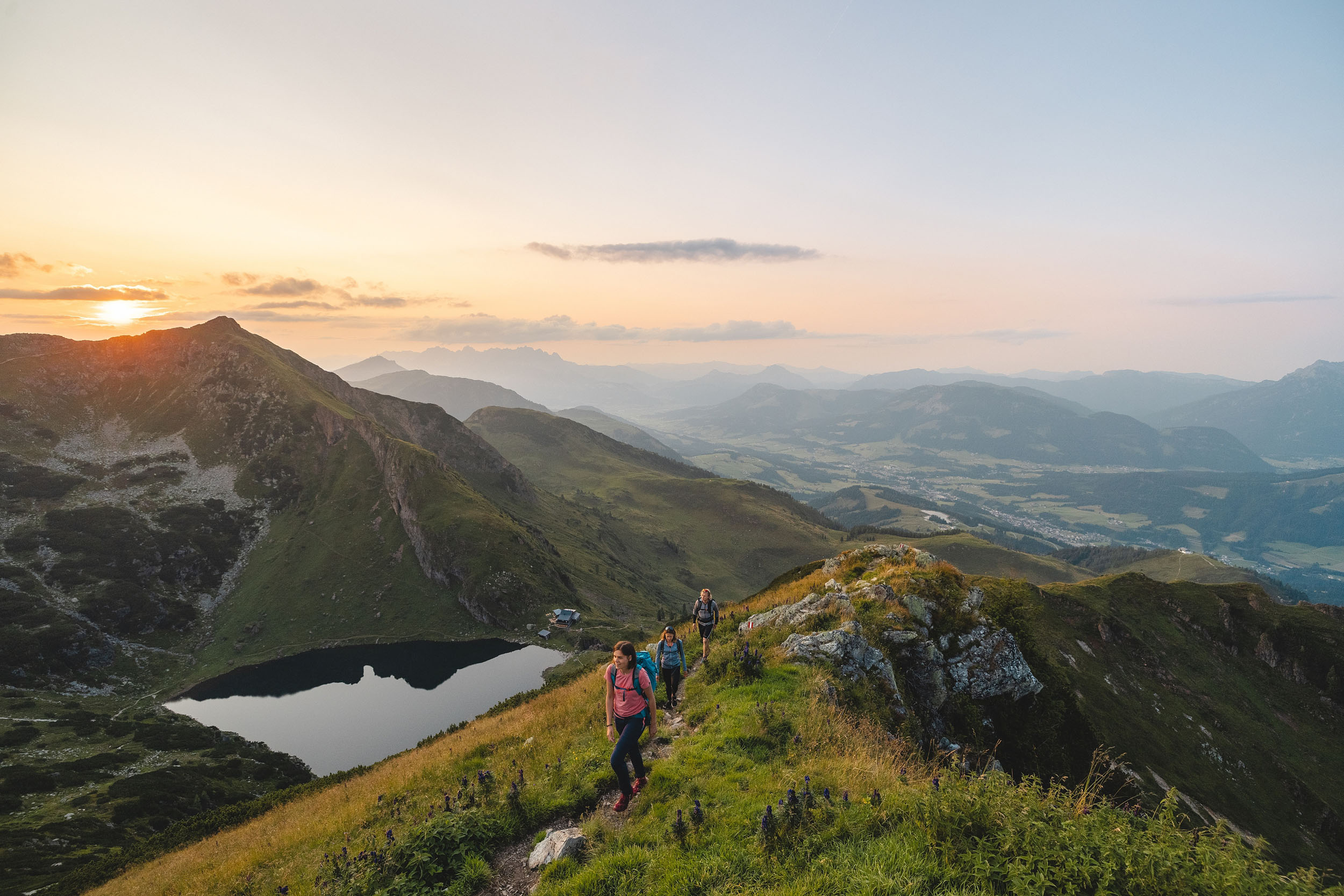 Wandergruppe auf dem Weg zum Gipfel der Henne, mit Blick auf den Wildseeloder, den Wildseelodersee und die Wildseeloderhütte im Abendlicht, umgeben von einer beeindruckenden Berglandschaft.