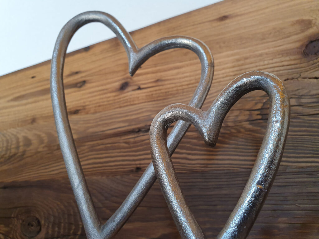 Zwei verbundene Metallherzen auf Holzbrett symbolisieren Liebe zum Detail