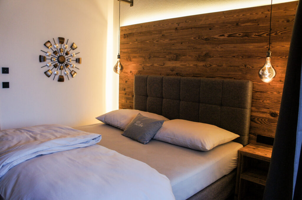 Doppelbett mit Holzrückwand, zwei Hängelampen und dekorativem Kissen in modern-alpinem Schlafzimmer