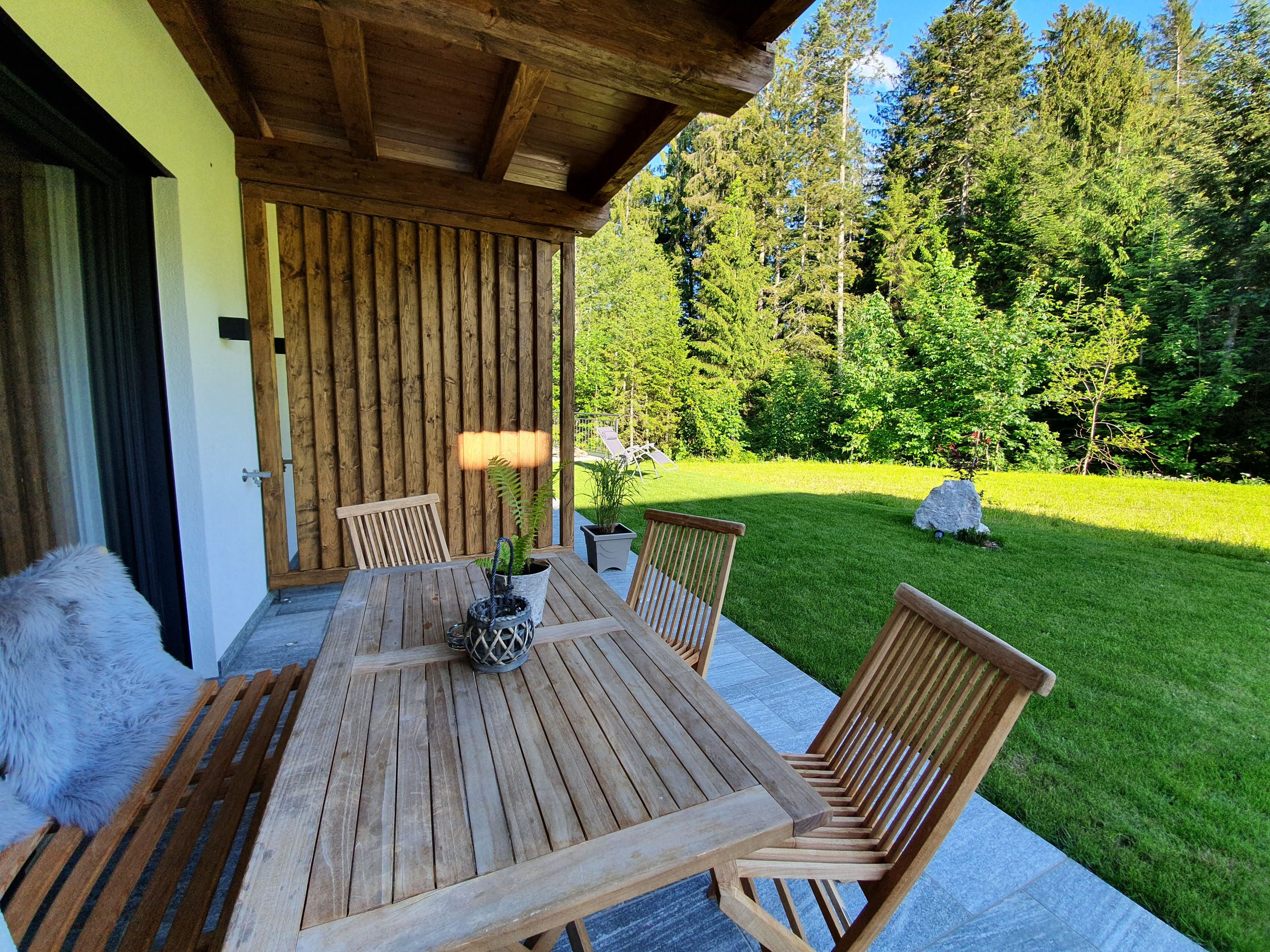 Holzterrasse mit Esstisch, Liegestuhl und angrenzender Sommerwiese im Chalet