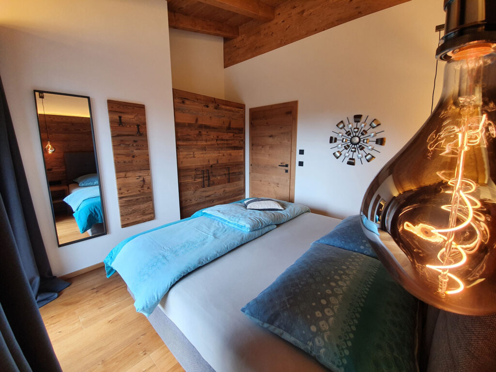 Boxspringbett, Designer-Leuchte und Spiegel unter Holzbalken