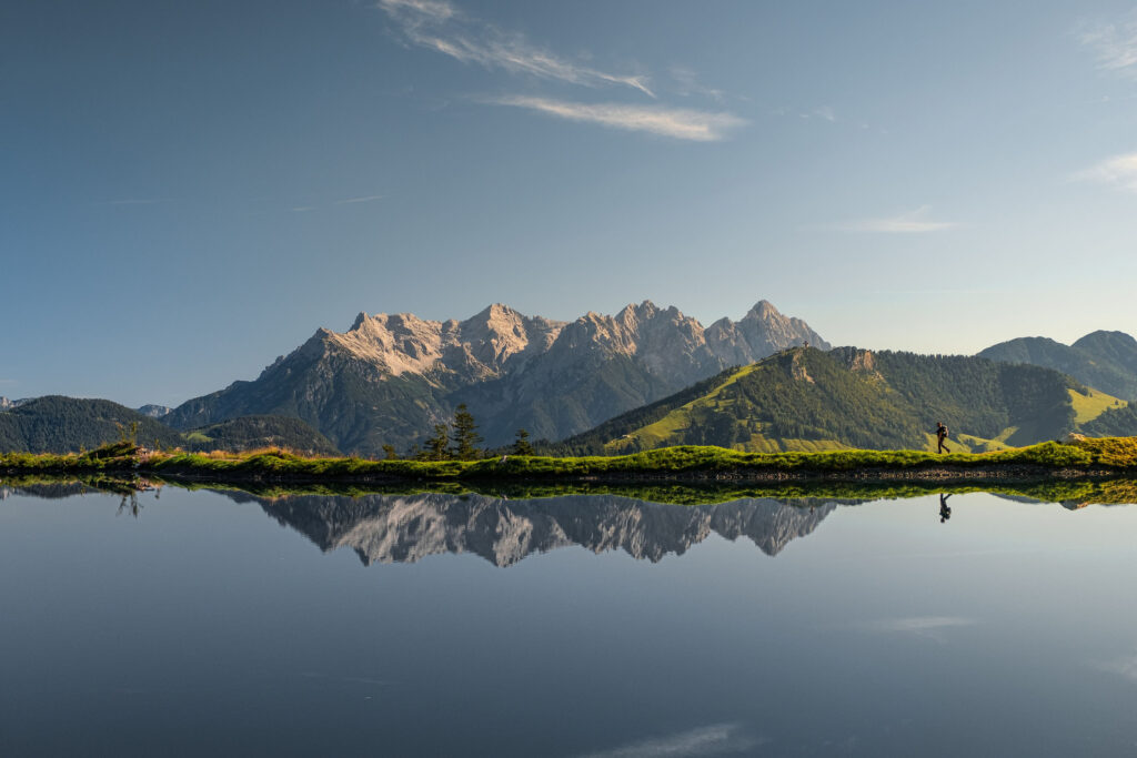 Ein Bergsee spiegelt die imposante Bergkette des Wilden Kaisers bei klarem Himmel und ruhiger Atmosphäre.