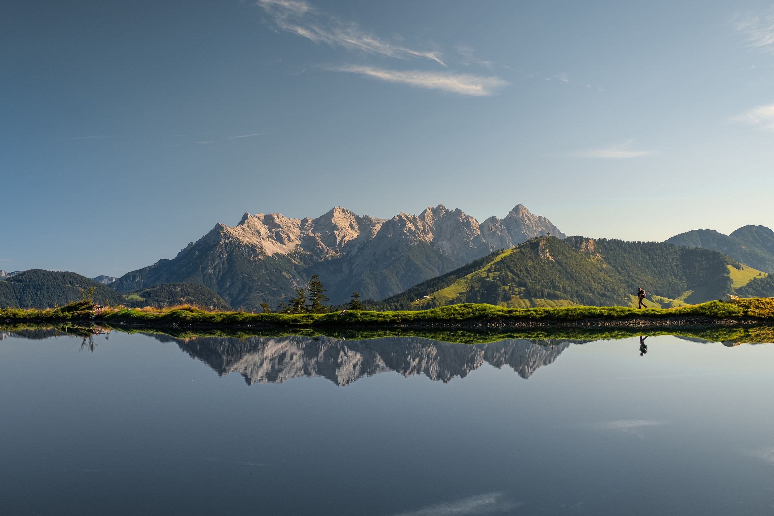 Ein Bergsee spiegelt die imposante Bergkette des Wilden Kaisers bei klarem Himmel und ruhiger Atmosphäre.