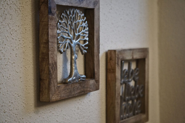 Wanddeko aus Holzrahmen mit silbernem Lebensbaum und Schriftzug „lebe liebe lache“ im alpinen Chalet-Stil.