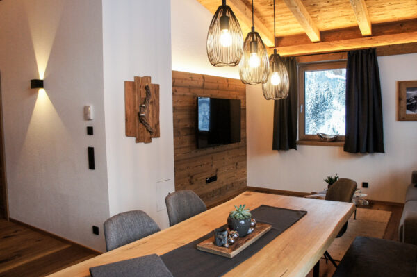 Essbereich mit Holzdecke, Hängelampen und TV an rustikaler Holzverkleidung, Fenster mit Blick auf verschneite Landschaft