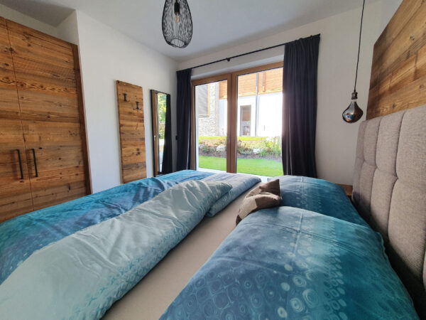 Boxspringbett mit türkis Decken, Panoramafenster und Altholzschrank im Chaletzimmer