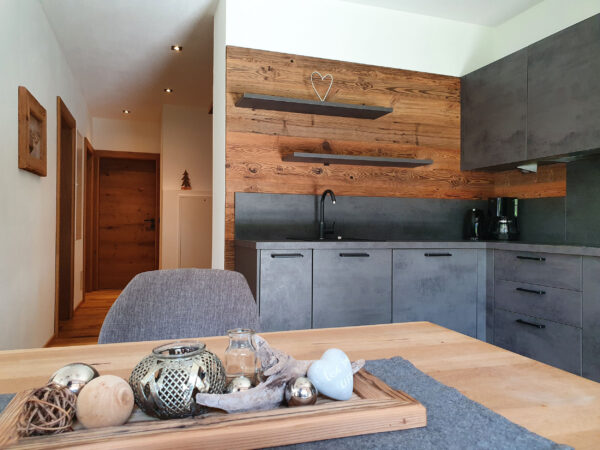 Offene Küche im Chalet mit Altholzwand, dunklen Schränken und Essbereich