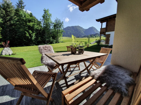 Überdachte Terrassenlounge mit Holztisch und Blick auf Wald und Garten
