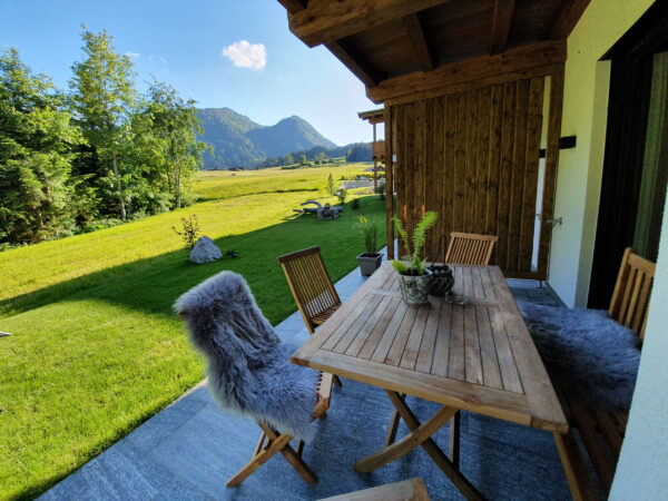 Holzbalkon-Lounge mit Tisch, Fellauflage und Blick auf Sommerwiese